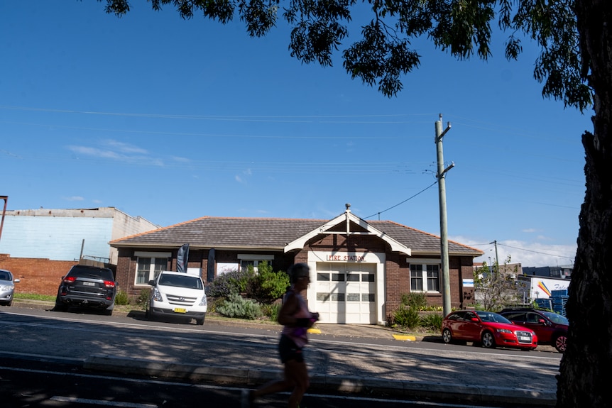 A wide shot of a woman running past an old fire house that is now a funeral home