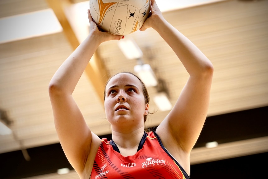 Isabella Ivancic-Holland holds a netball above her head about to shoot a goal.