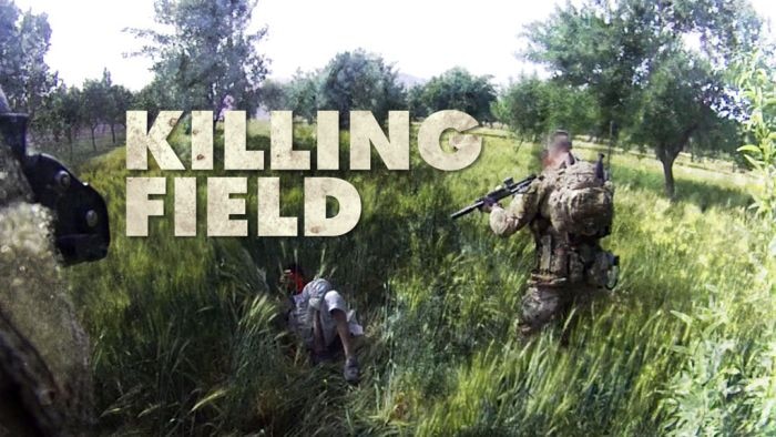 Soldier pointing a rifle at a person with their back on the ground in the middle of a field of tall grass