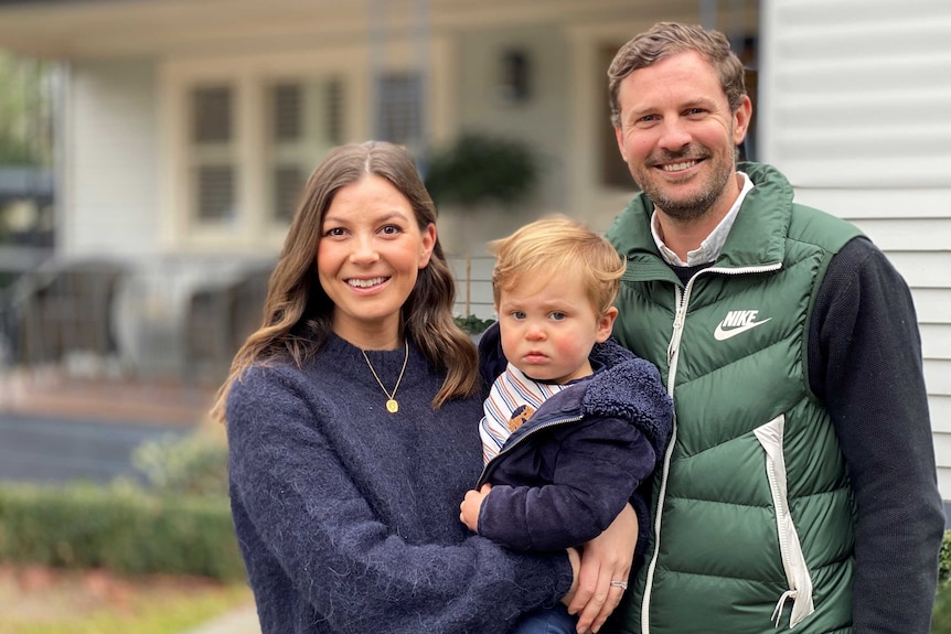 A man and a woman stand together holding their young son.