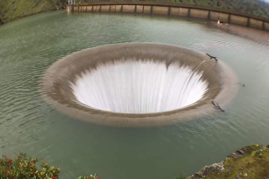 Water pours down a large hole in the middle of a lake.