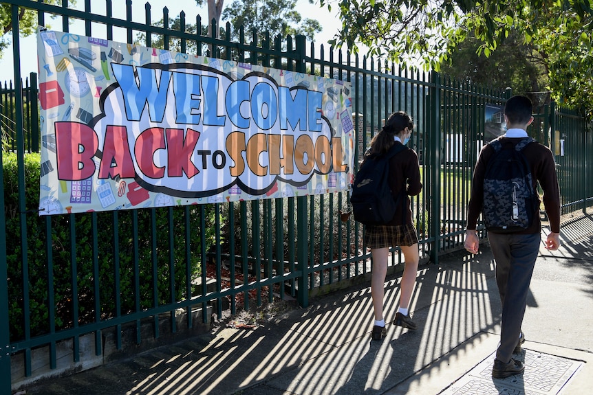 two students walking outside a school with a sign that reads welcome back