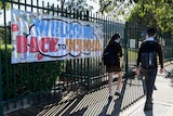 Students walking past a banner hanging on a fence that reads "Welcome Back to School"
