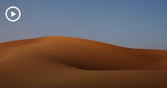 A large orange hill of sand set against a blue sky backdrop.