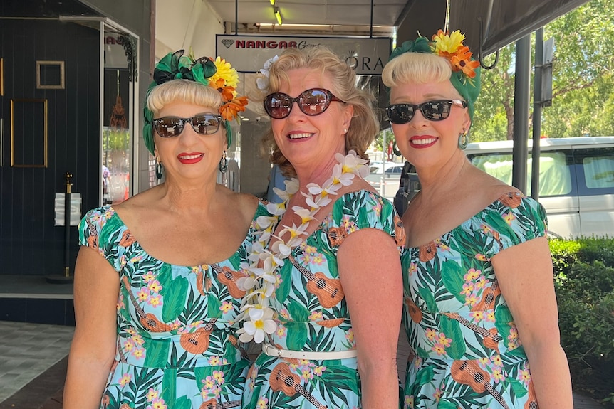 three women wear green Hawaiian themed dresses and leis 