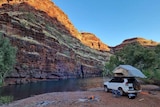 A car, tent and campfire set up with the backdrop of a gorge and water. 
