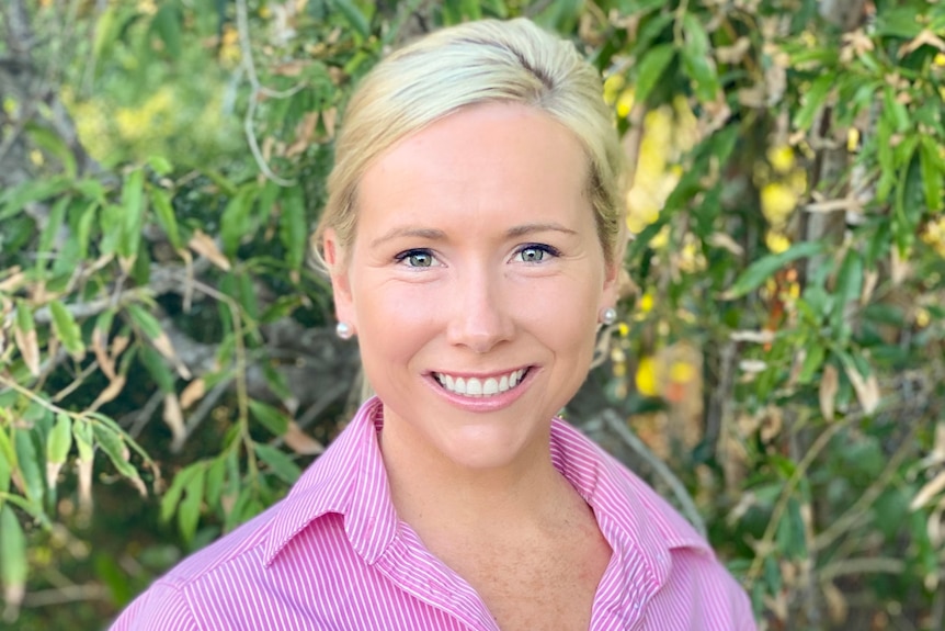 Woman in pink shirt smiles at camera with greenery behind her