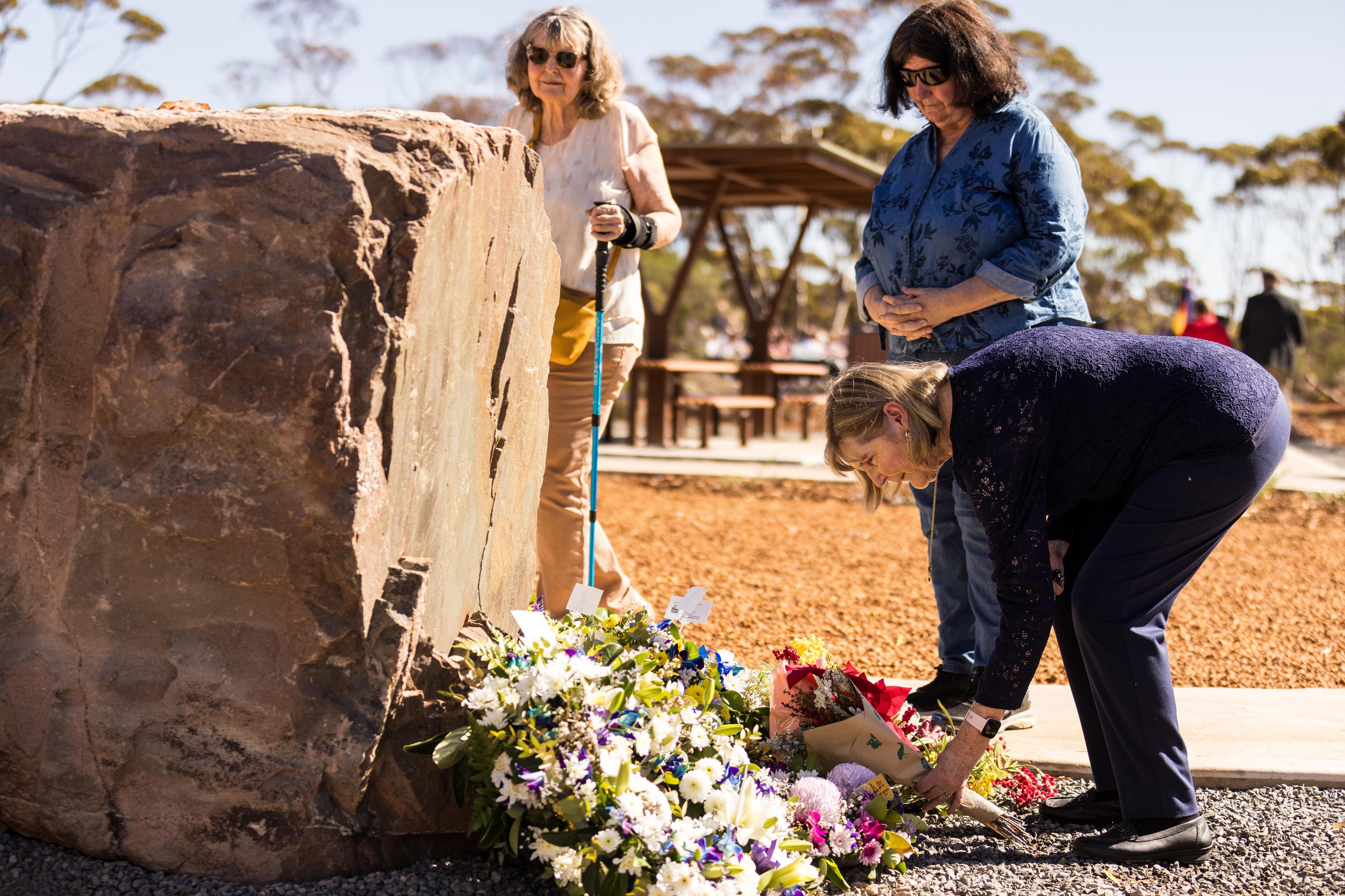 A woman lays flowers at a memorial while two other women look on.  