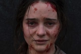 A young woman covered in blood faces the camera