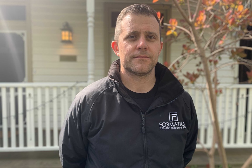 Landscaper Chris Weiss, a man with short brown hair, stands outside of a house in the sunshine.