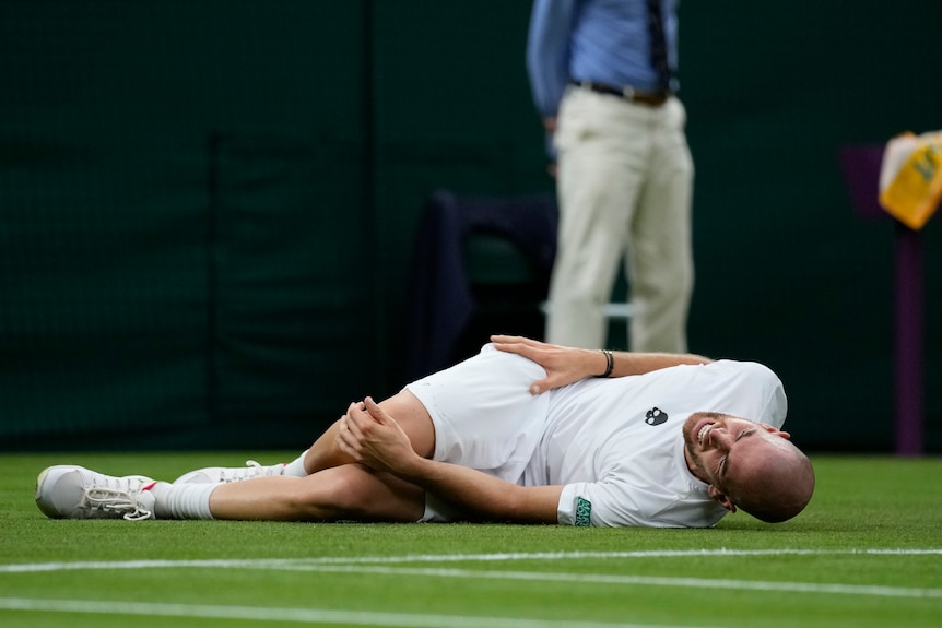 A male tennis player lies on Centre Court clutching his knee in pain during a match at Wimbledon.