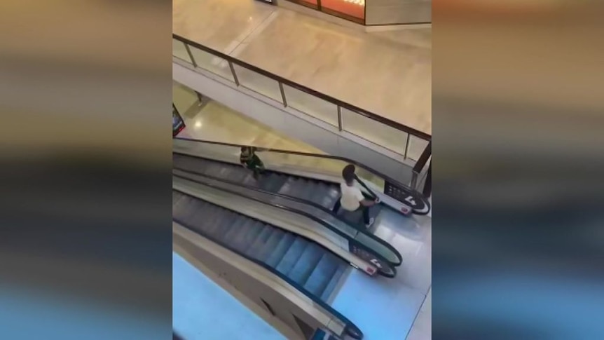 Mobile vision shows a man at the top of an escalator brandishing a bollard as a man approaches him.