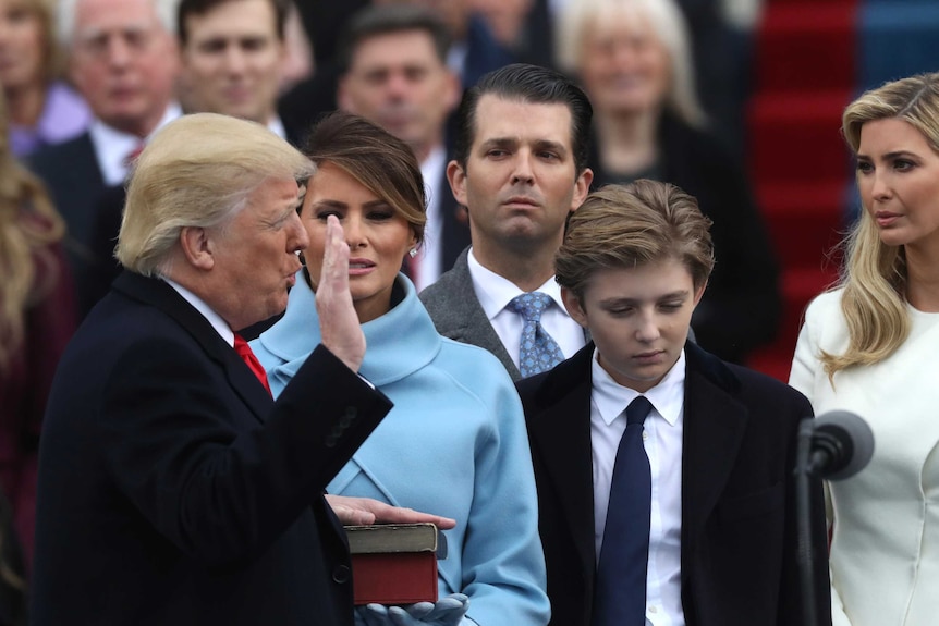 Donald Trump raises his right hand and speaks an oath with his other hand on a book held by wife Melania Trump