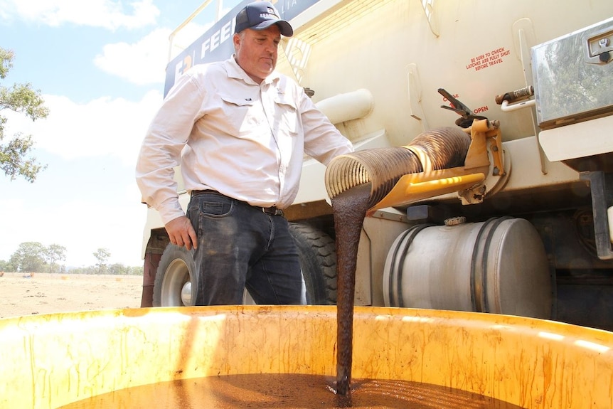Tony Newman stands next to a truck as brown molasses pours out of a tube and into a bucket.