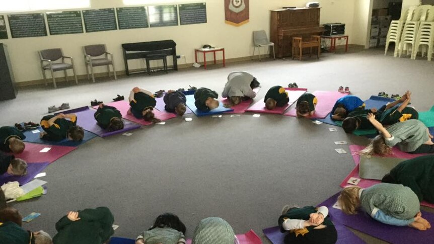 Students tucked into balls on yoga mats placed in a circle.