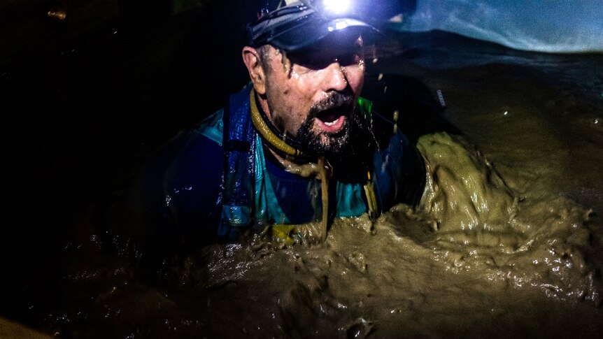 Man with a headlamp, at night in a pool of mud looking in shock.