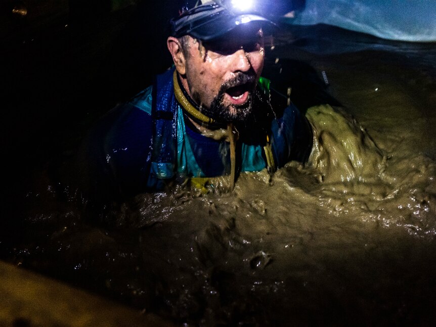 Man with a headlamp, at night in a pool of mud looking in shock.
