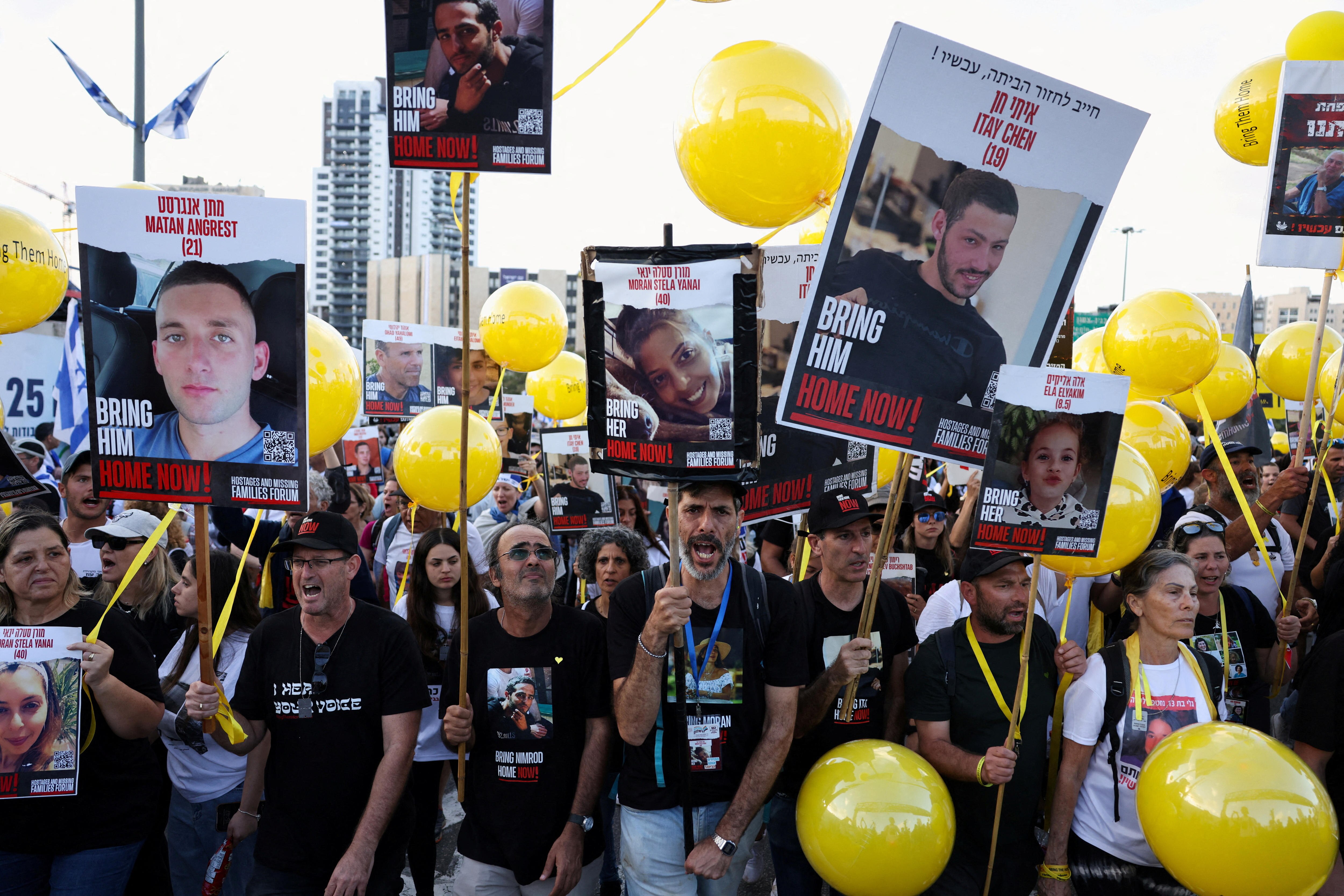 protest of people holding up placards of pictures of hostages, with yellow balloons