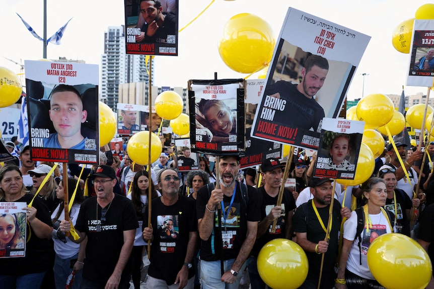 protest of people holding up placards of pictures of hostages, with yellow balloons