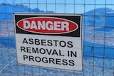 A sign on a fence saying 'Danger, asbestos removal in progress'