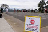 A sign reading 'please help stop the spread of virus' in front of a regional netball match being played.