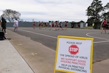 A sign reading 'please help stop the spread of virus' in front of a regional netball match being played.