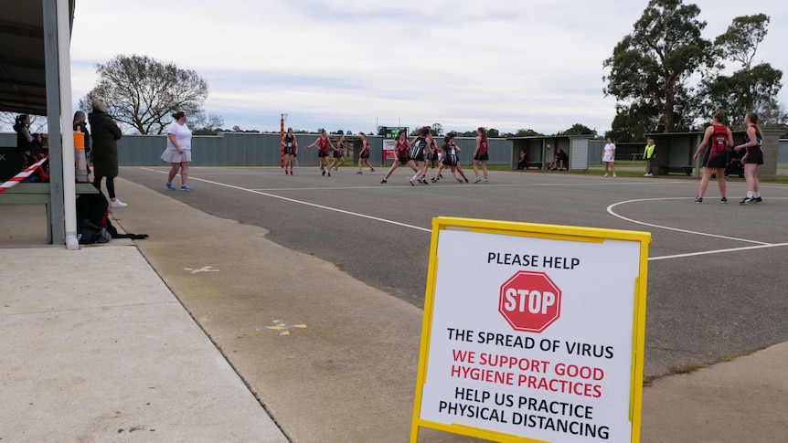 A sign reading 'please help stop the spread of virus' in front of a regional netball match being played.