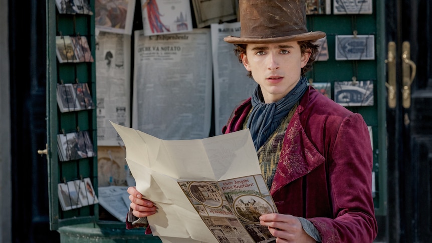 Timothée Chalamet dressed as Wonka looks up from reading a parchment paper on set of the film Wonka.
