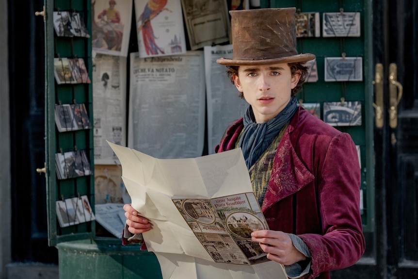 Timothée Chalamet dressed as Wonka looks up from reading a parchment paper on set of the film Wonka.