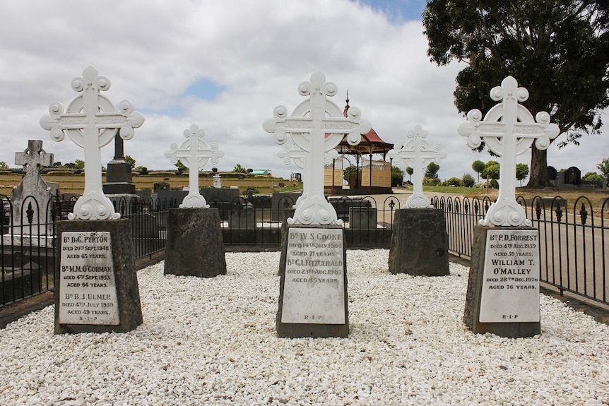 Three graves with white Celtic crosses sitting on white crushed rock.