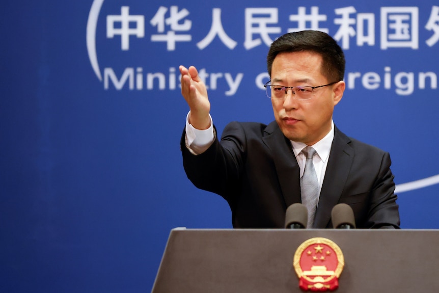 A Chinese man raises his hand at a lectern