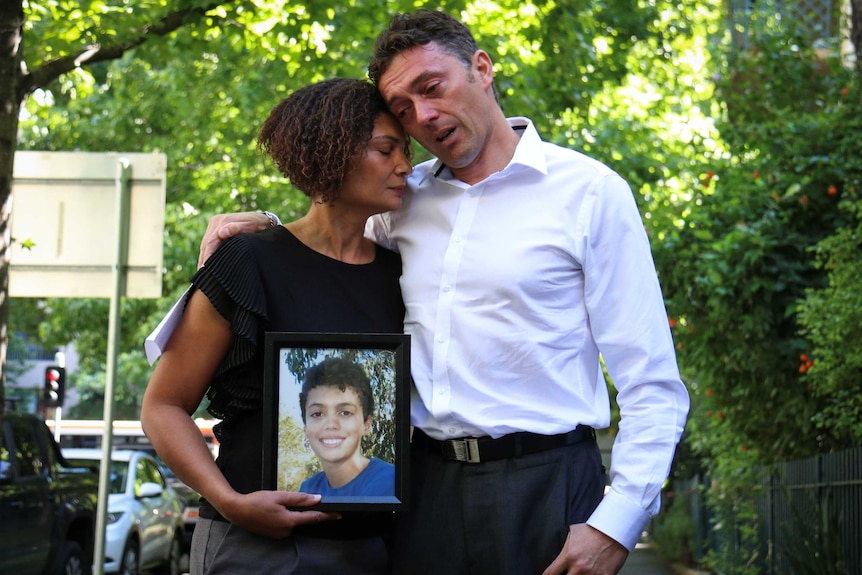 Gabrielle Catan holding a photo of her dead son Louis Tate while embracing husband Simon Tate.