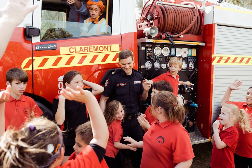 A wide shot of firefighter Michael Hatfield next to a fire truck with students from Mosman Park School for Deaf Children.