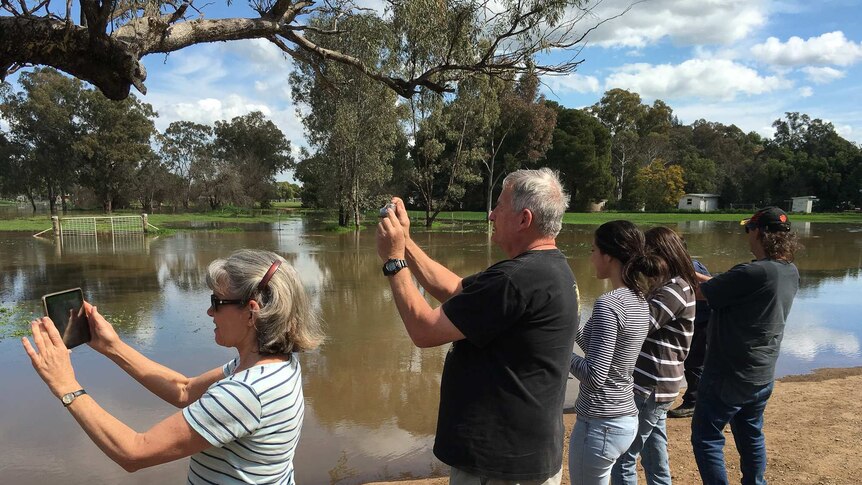 People standing in a row taking pictures of flooded land