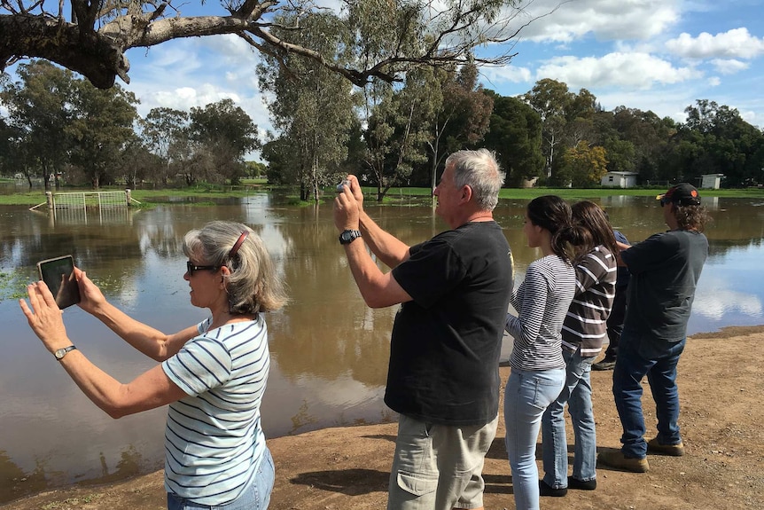 People standing in a row taking pictures of flooded land