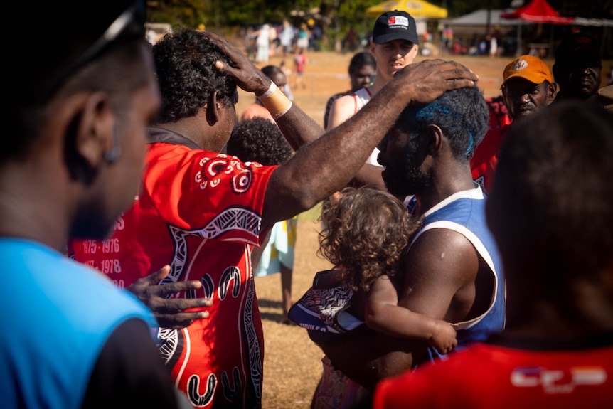 Two men wearing jerseys from different teams placing their hands on each others heads in a friendly way