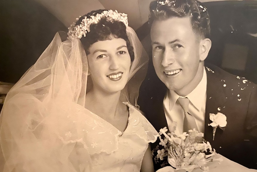 A black and white photo of a young woman and man on their wedding day smiling at the camera