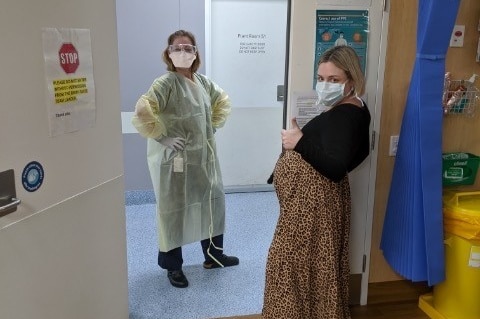 A midwife in full PPE with a heavily pregnant woman wearing a mask.