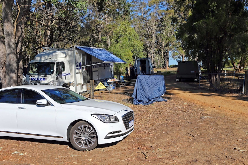 A white unmarked vehicle parked in front of a police mobile command centre