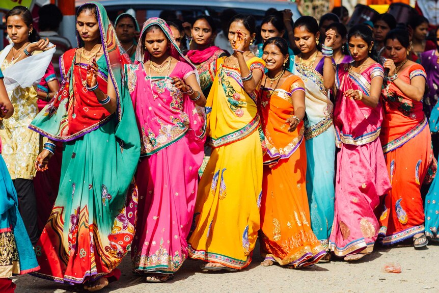 Women stand in a line wearing saris in a myriad of colours.