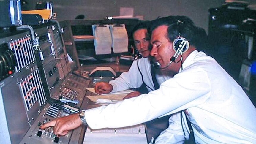 Two men wearing headsets sit at an operations console