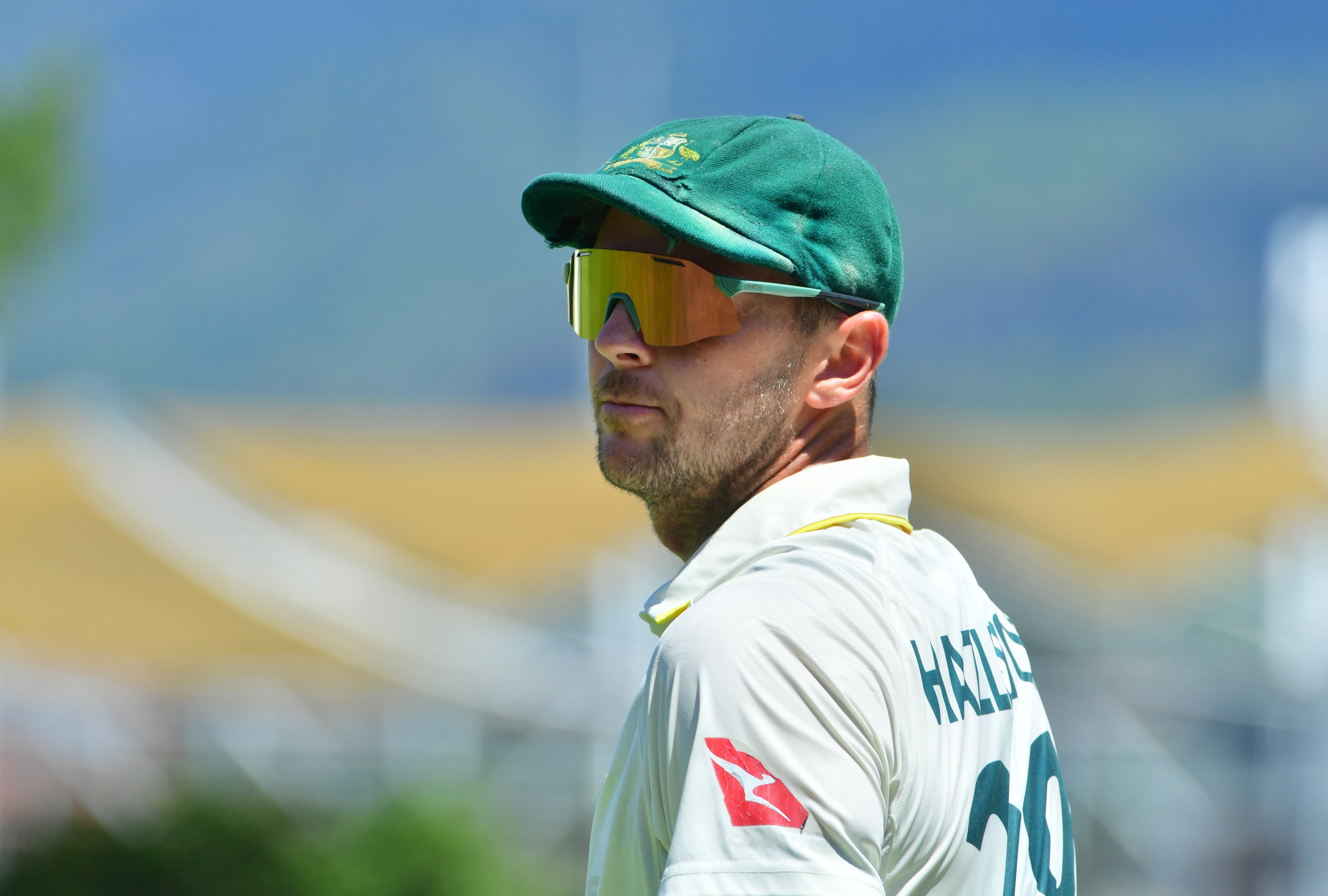 An Australian fast bowler wearing dark glasses and his Baggy Green looks serious between deliveries.