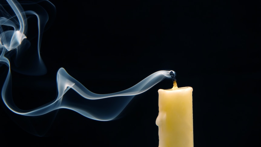 Smoke rises from the wick of a slender candle that has just been snuffed out.