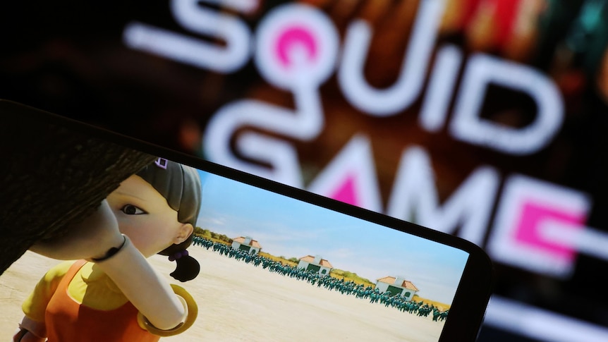 The Netflix series "Squid Game" is played on a mobile phone with the squid game logo appearing in the background