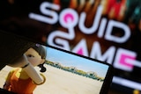 The Netflix series "Squid Game" is played on a mobile phone with the squid game logo appearing in the background