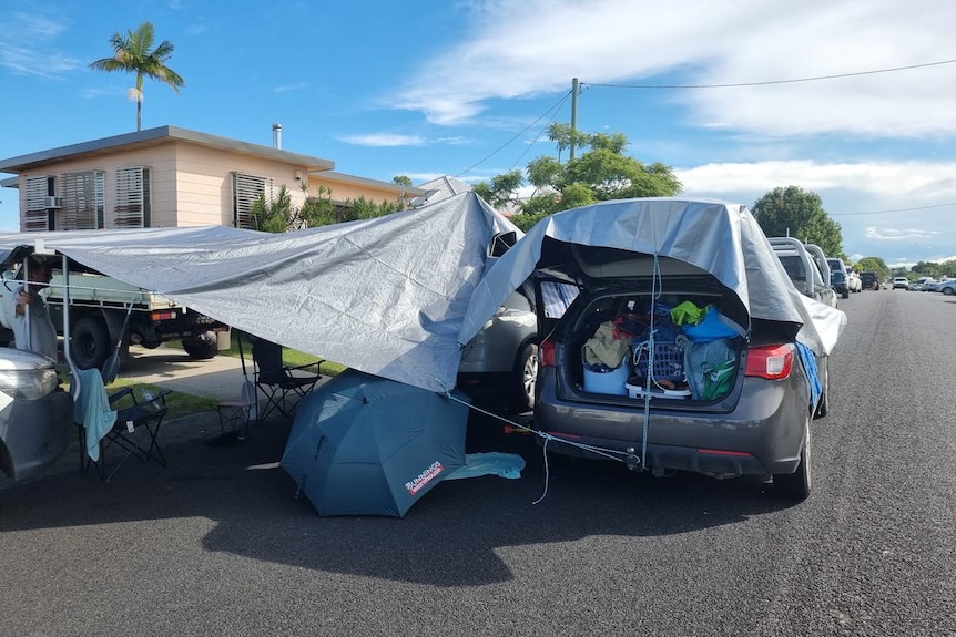 A car with full boot and make shift tent off the side using a tarp.