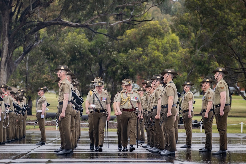 Several people lined up wearing beige uniforms with Army medals