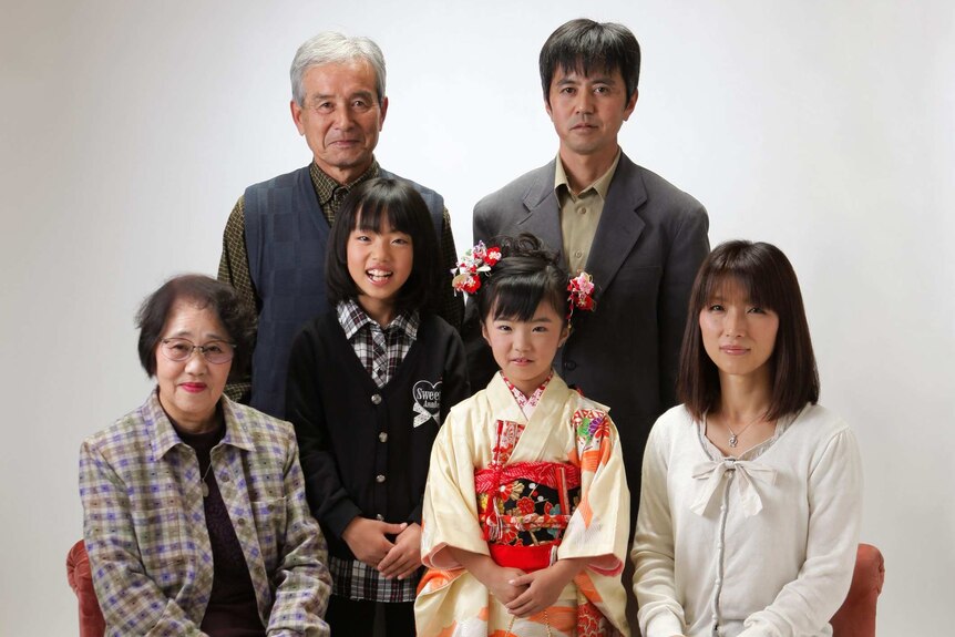 A little girl in a traditional Japanese kimono, surrounded by her family in a white photography studio