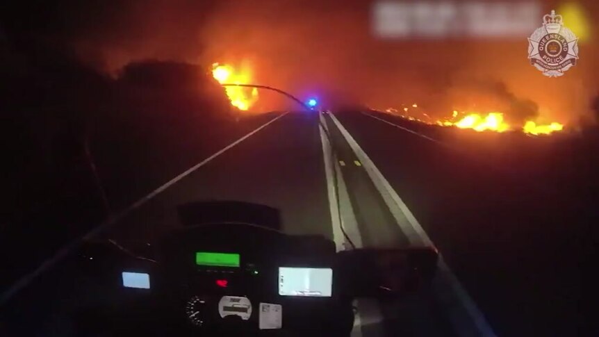 A view over a motorcycle windscreen shows flames on either side of the road.
