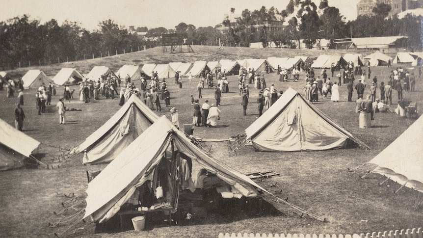 A black and white image of dozens of white tents set up on an oval with people milling about